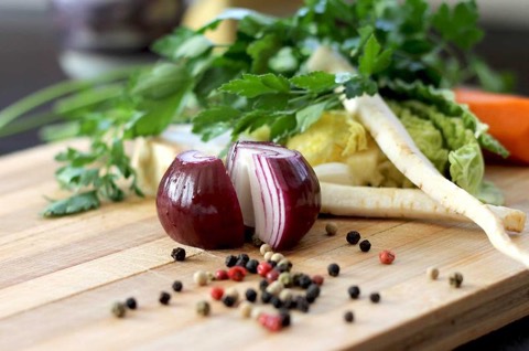 Vegetables and peppercorns on a chopping board.